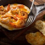 Braised prawns with shells attached in a mini serving pan. Bread at the side