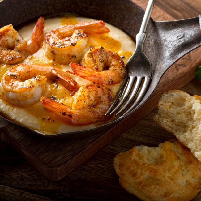 Braised prawns with shells attached in a mini serving pan. Bread at the side