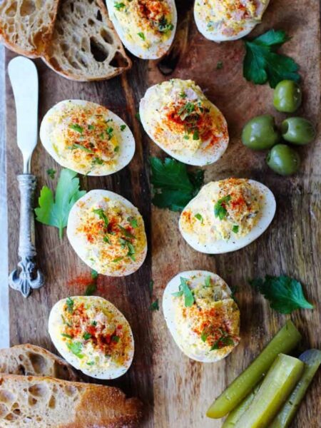 Stuffed or deviled eggs served on a wooden board with bread and green vegetables for garnish