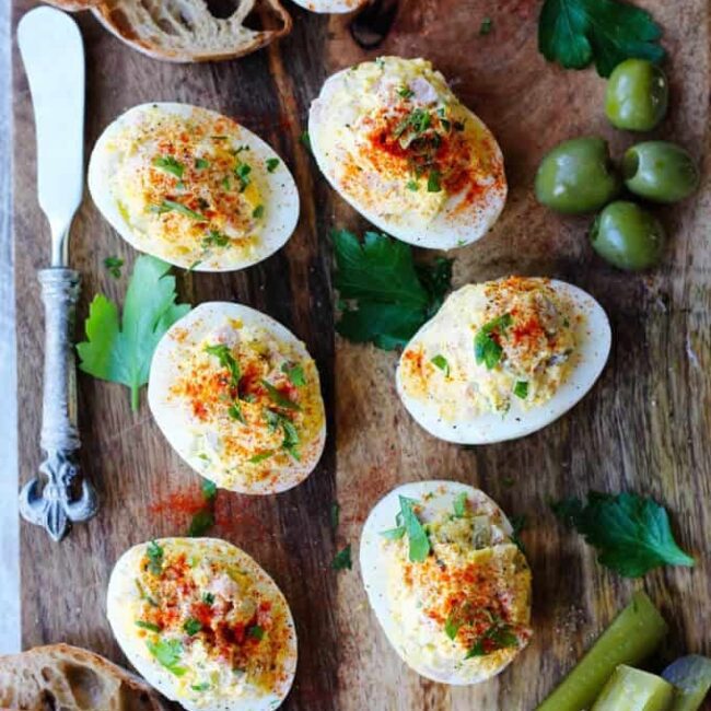 Stuffed or deviled eggs served on a wooden board with bread and green vegetables for garnish