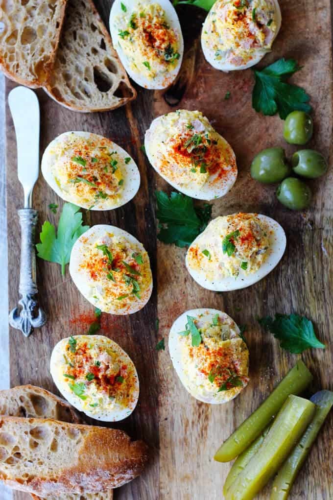 Stuffed or deviled eggs served on a wooden board with bread and green vegetables for garnish