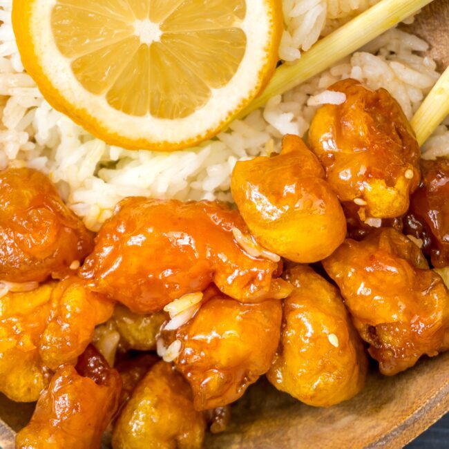 Chinese Chicken in Lemon Sauce served in a wooden bowl with chopsticks. Lemon wheel as garnish