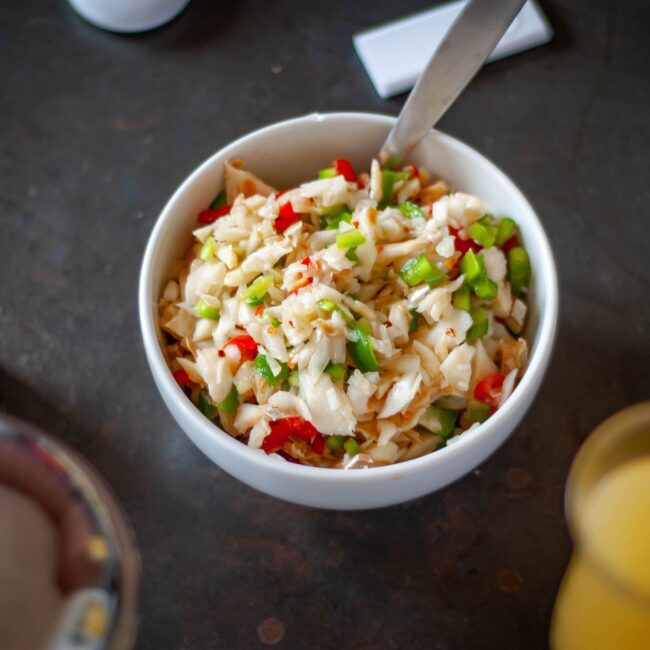 Saltfish buljol served in a white bowl with pepper sauce bottle to the side