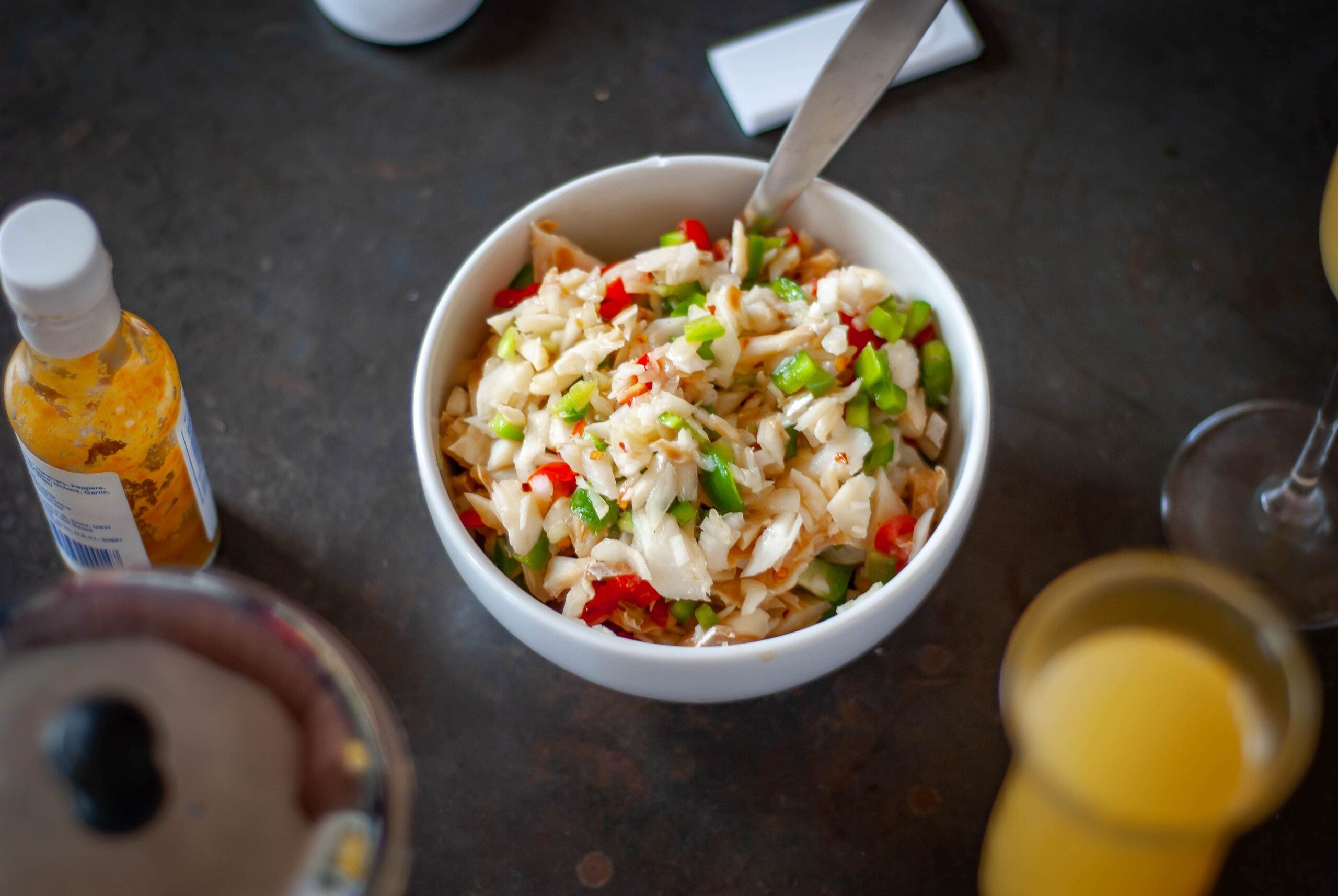 Saltfish buljol served in a white bowl with pepper sauce bottle to the side