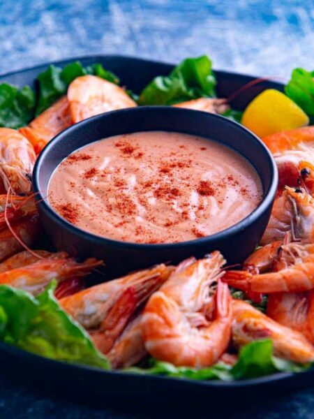 Seafood sauce served in a bowl placed on a plate. Prawns are served on the plate and around the bowl