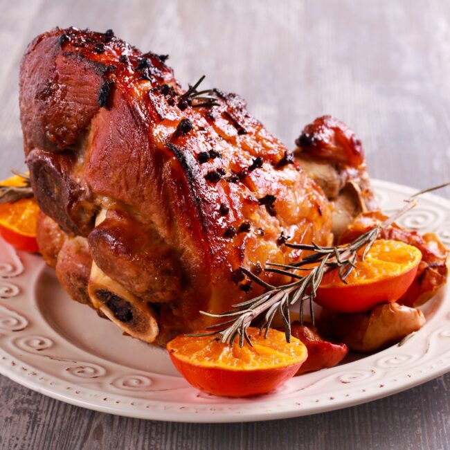 Spicy Orange Gammon Bake served on a white plate; garnished with baked oranges